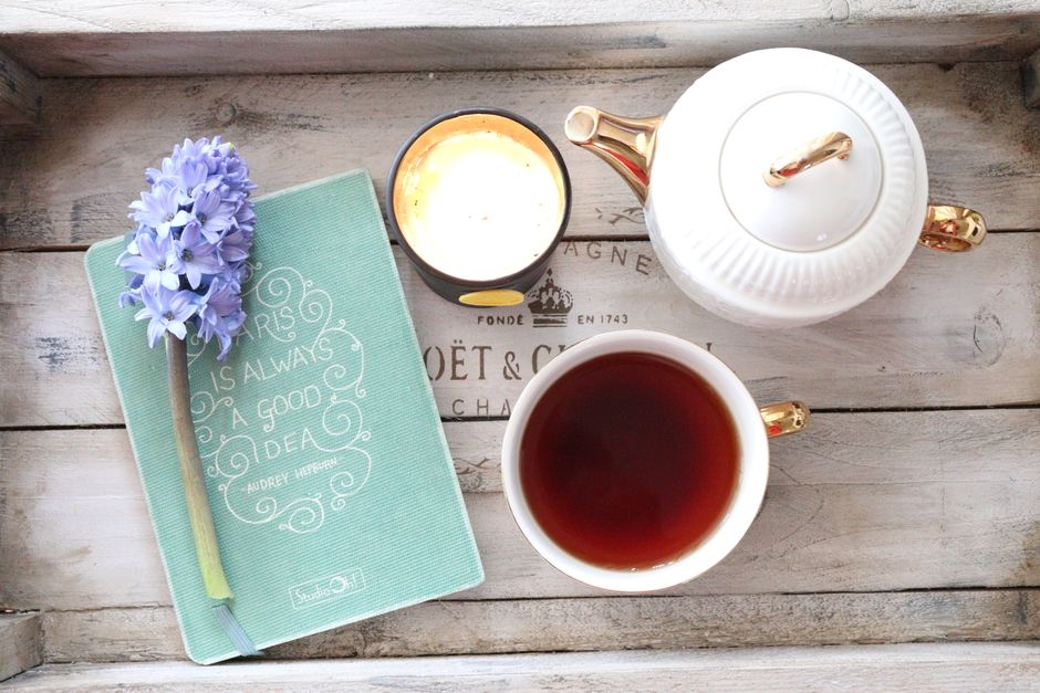 Charming flat lay of tea, notebook, candle, and flower on rustic table.